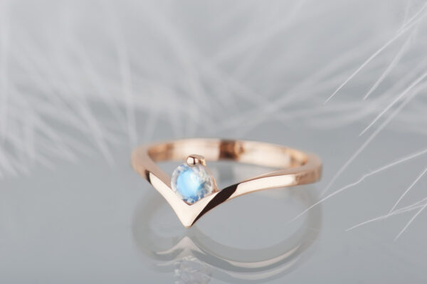 Pierścionek z różowego złota 585 z niebieskim kamieniem księżycowym. Szyna wygięta w kształcie litery v. Okrągły kamień oprawiony w miejscu wcięcia.