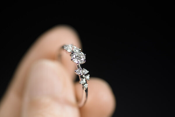 Pierścionek zaręczynowy z białego złota z brylantem 0,3 ct i małymi diamentami po bokach trzymany w palcach