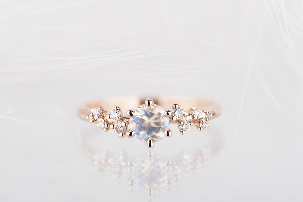 Pierścionek z różowego złota próby 585 z niebieskim kamieniem księżycowym i małymi diamentami po bokach. Zdjęcie wykonane w studiu na białym tle w lampach błyskowych