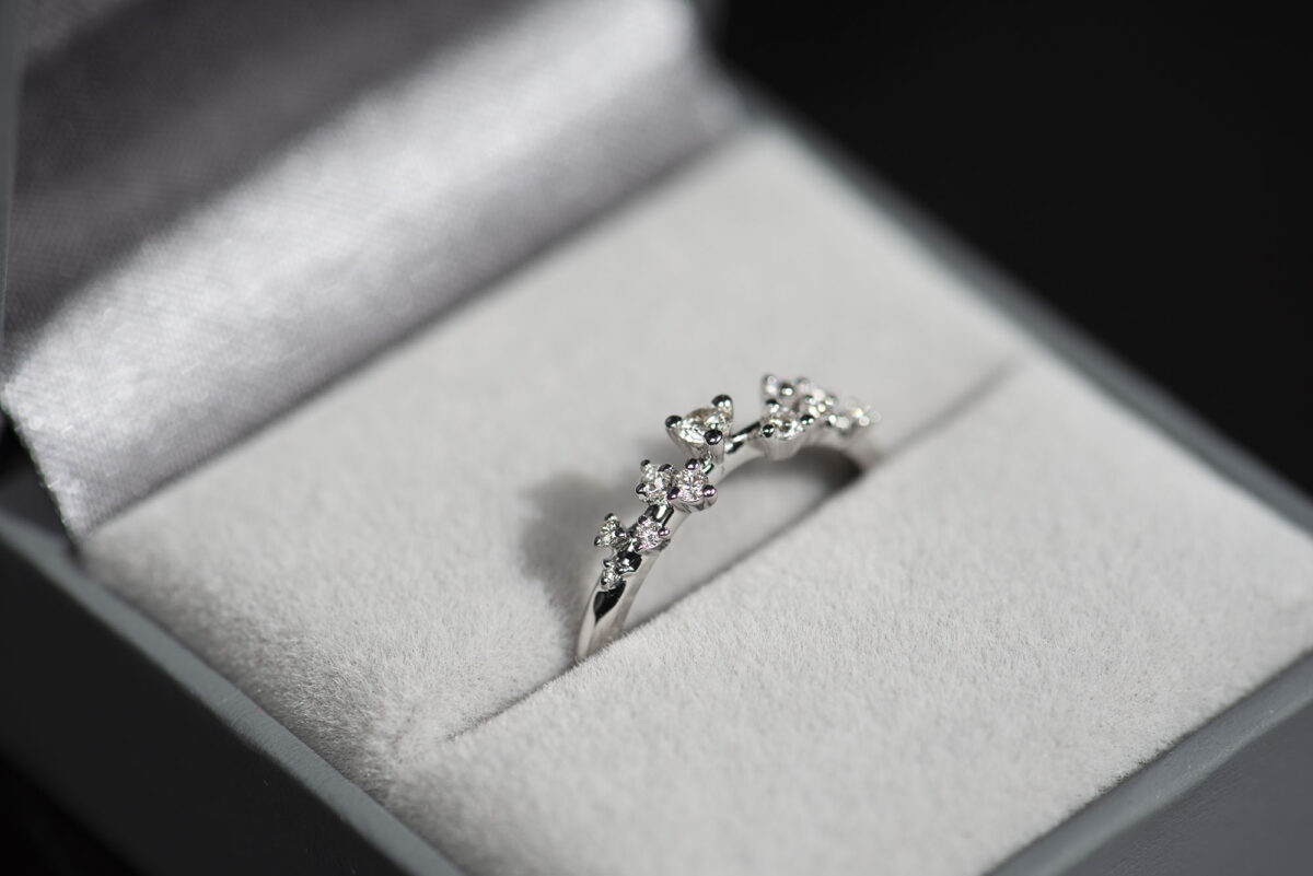 Pierścionek z białego złota z drobnymi diamentami sfotografowany w szarym pudełku na biżuterię.