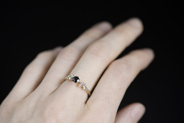 Pierścionek zaręczynowy ze złota próby 585 z czarnym diamentem i drobnymi białymi diamentami po bokach założony na palec. Zdjęcie wykonane w naturalnym oświetleniu
