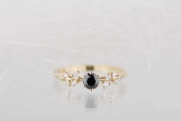 Pierścionek zaręczynowy ze złota próby 585 z czarnym diamentem i drobnymi białymi diamentami po bokach. Zdjęcie wykonane na białym tle w studio w świetle lamp błyskowych