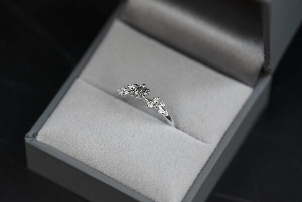 pierścionek zaręczynowy z białego złota z głównym kamieniem diamentem sól i pieprz o macie 0,3 karata i oprawionymi po bokach białymi diamentami. Pierścionek umieszczony w szarym pudełku na biżuterię. Zdjęcie wykonane w rozproszonym świetle